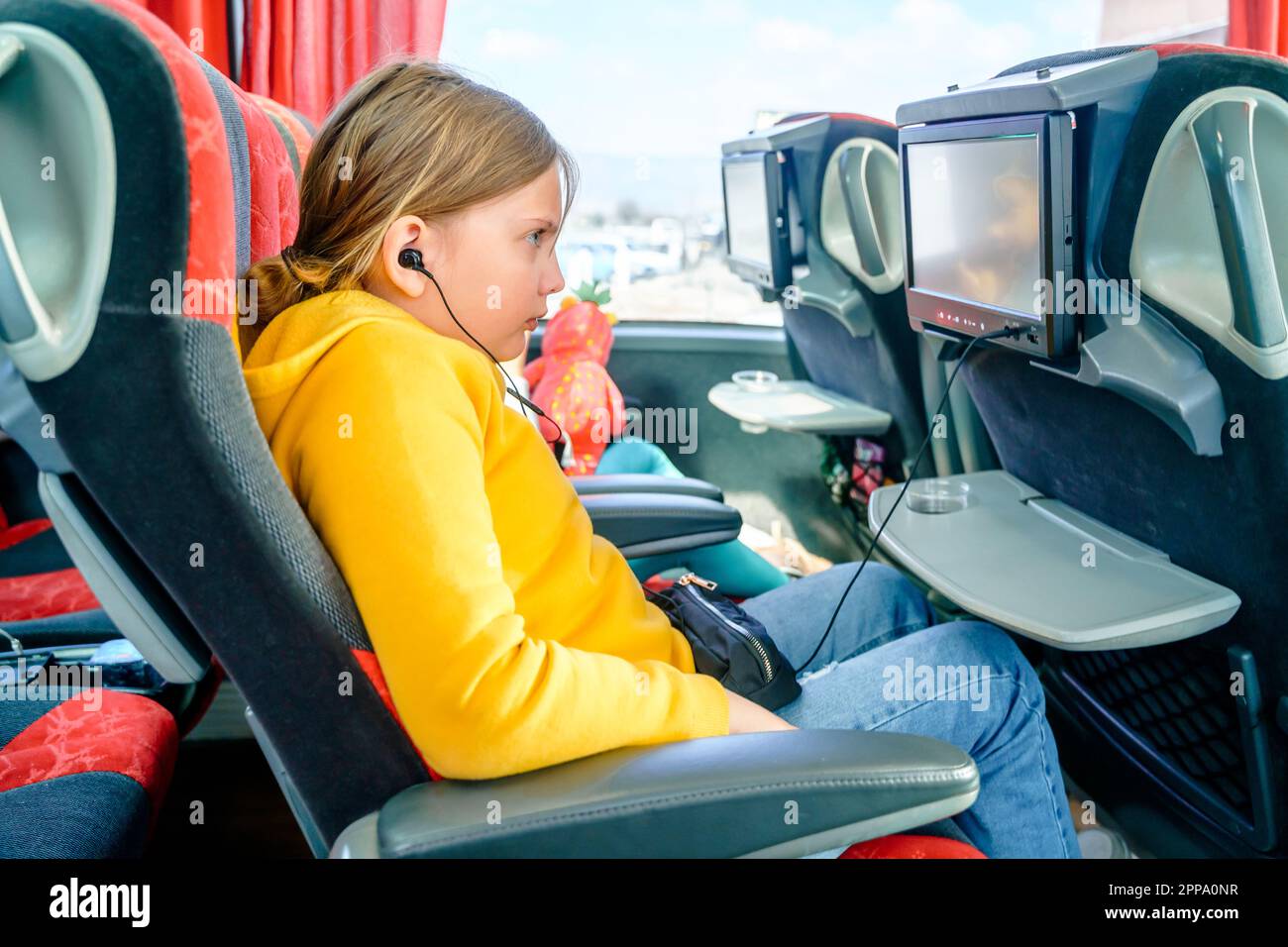 Autobus strada in viaggio. Girl kid ride a bordo di un grande e comodo autobus turistico. Guardare film cartoon sullo schermo in sedia. Sistema multimediale di intrattenimento Foto Stock