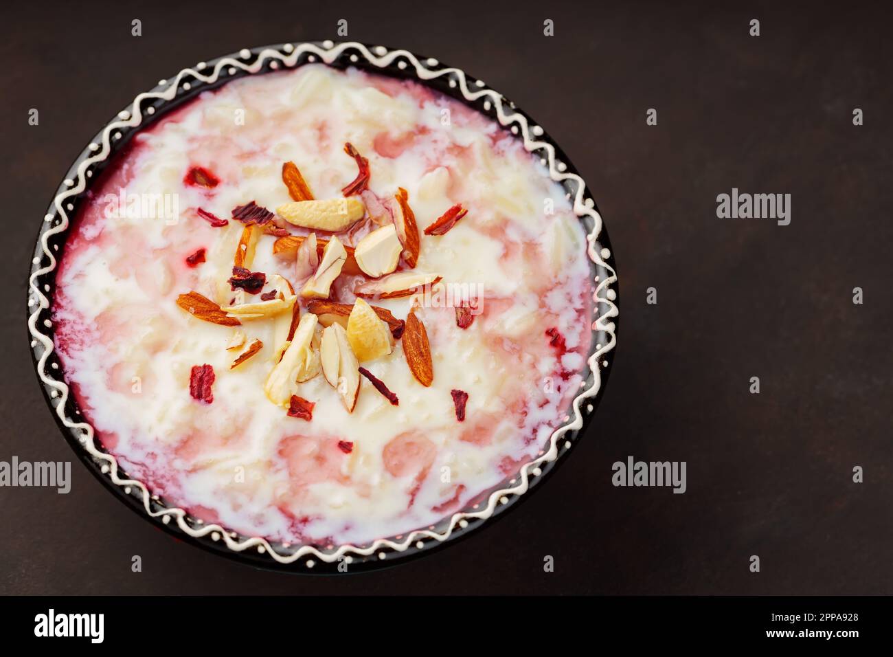 Budino di riso kheer indiano con noci su fondo scuro. Delizioso budino di riso con acqua di rosa. Spazio di copia. Vista dall'alto Foto Stock