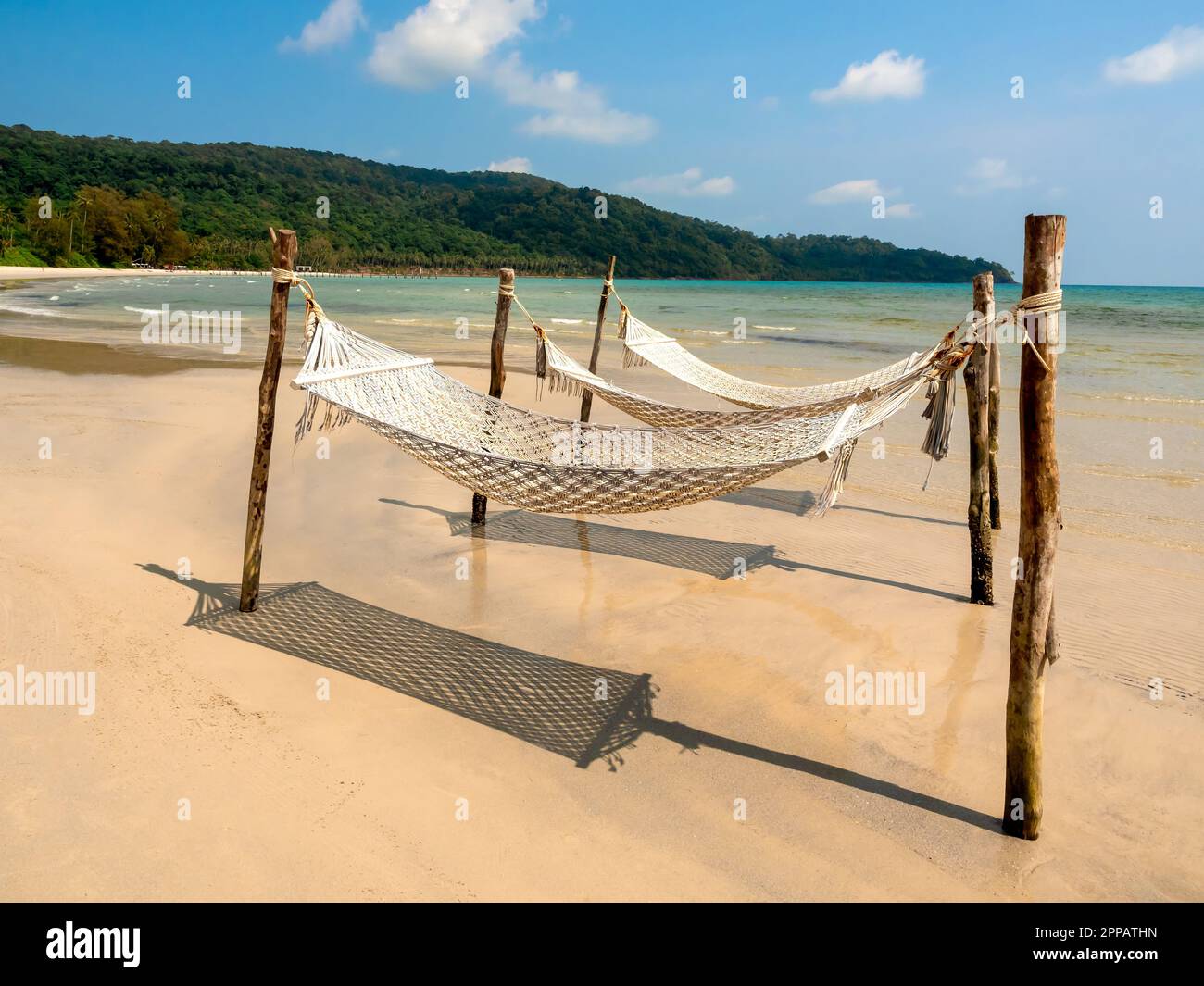 Due cradle di corda vuote appese ai pali di legno sulla spiaggia sabbiosa sul mare, isola e sfondo cielo blu. Rilassante culla a sospensione doppia o letto ad altalena Foto Stock