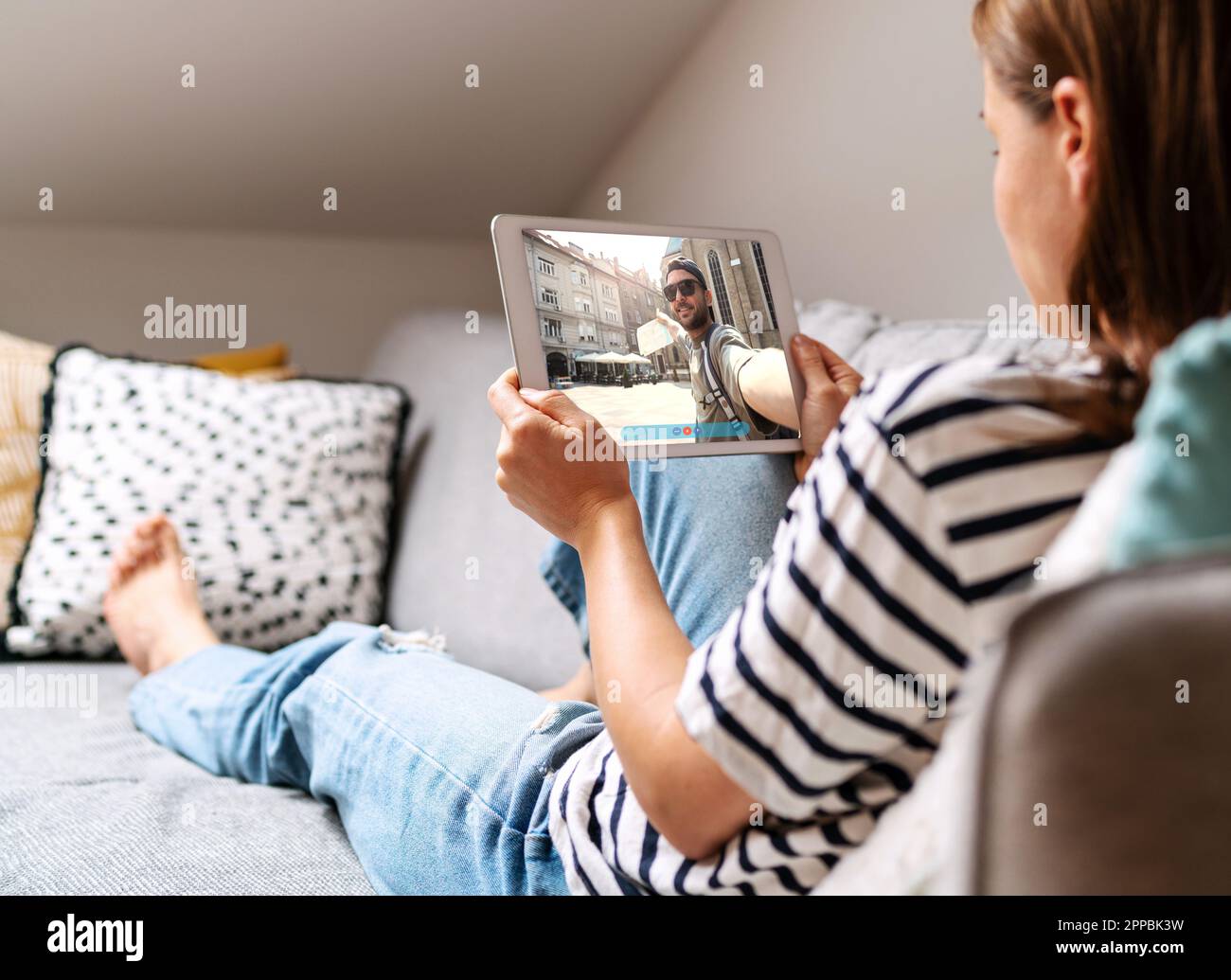 Uomo che viaggia e chiama la sua ragazza in video. Donna sdraiata sul divano a casa e in chat con il suo ragazzo online utilizzando un tablet digitale. Foto Stock