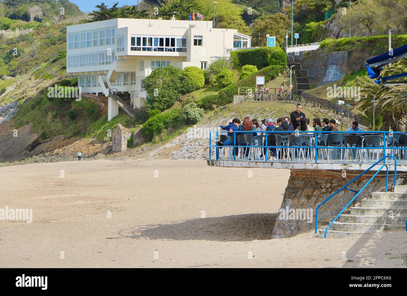 La gente che mangia su una terrazza ristorante all'aperto che sovrasta la spiaggia in un pomeriggio di primavera soleggiato Comillas Cantabria Spagna Foto Stock