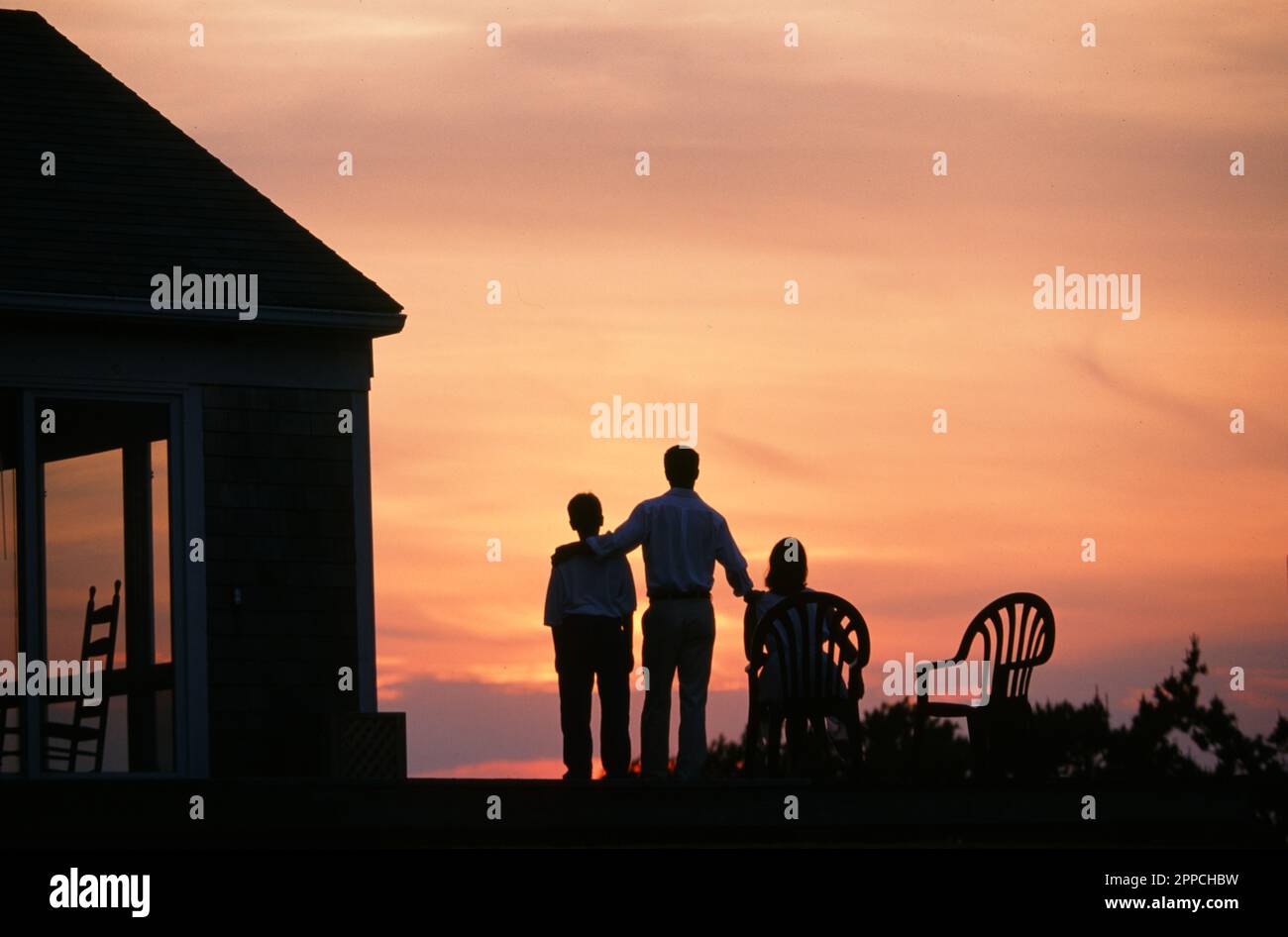 Famiglia di tre silhouette contro un bellissimo tramonto OH relax sul ponte del loro HomeNo Foto Stock