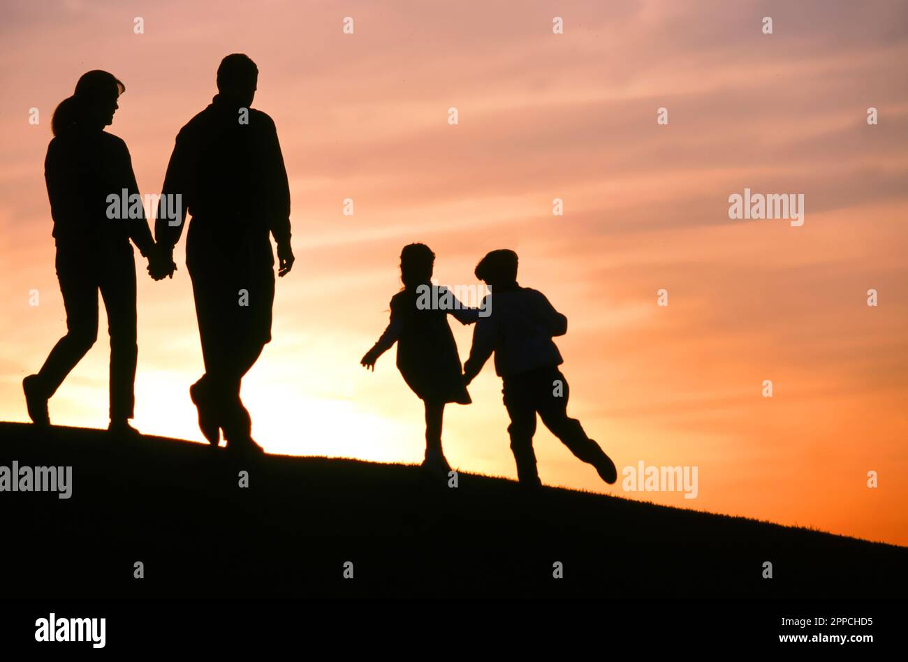 Silhouette di una famiglia che cammina insieme su una collina al tramonto Foto Stock