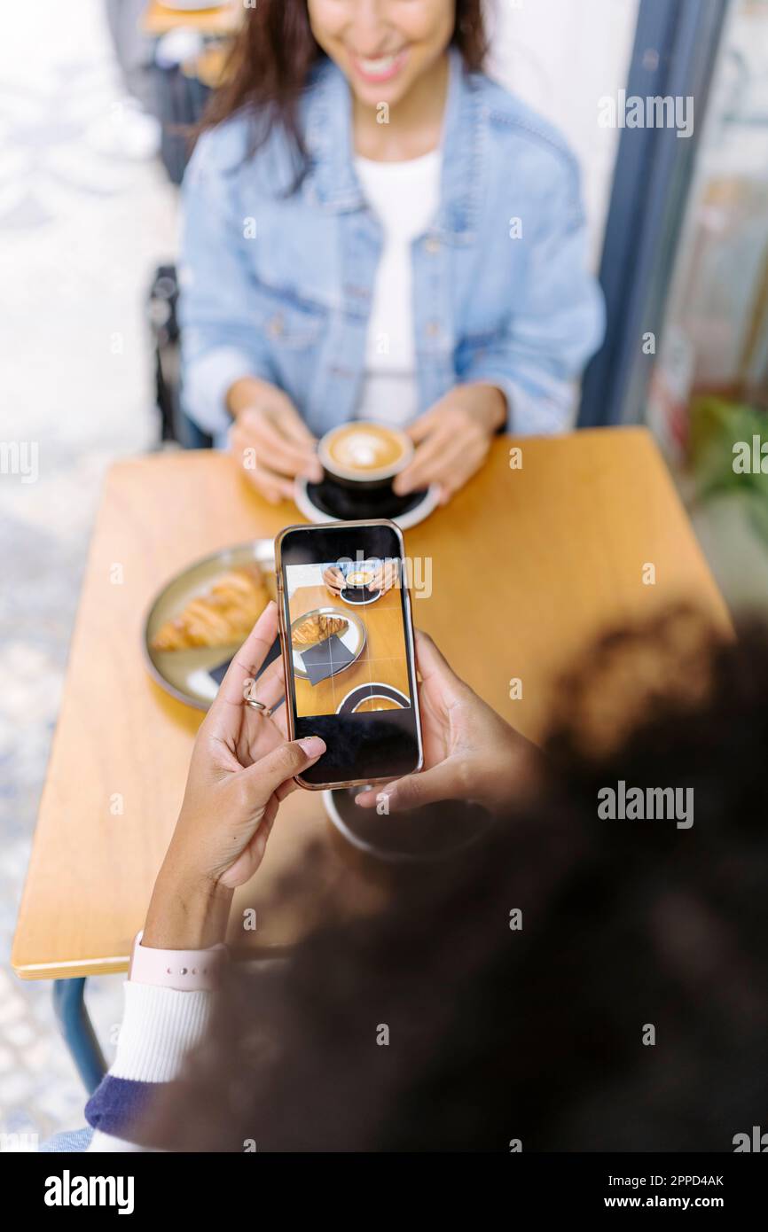 Giovane donna che fotografa cibo e bevande tramite smartphone Foto Stock