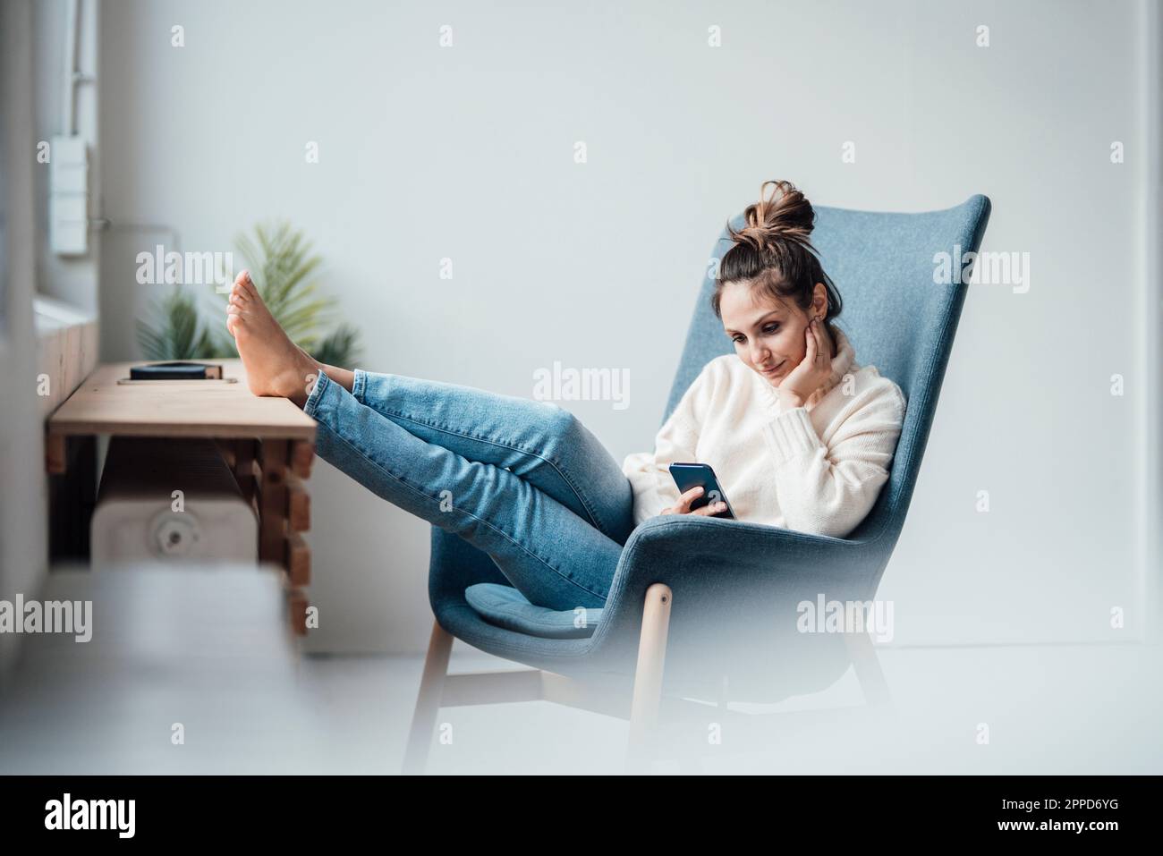 Giovane donna che usa uno smartphone seduto in poltrona a casa Foto Stock