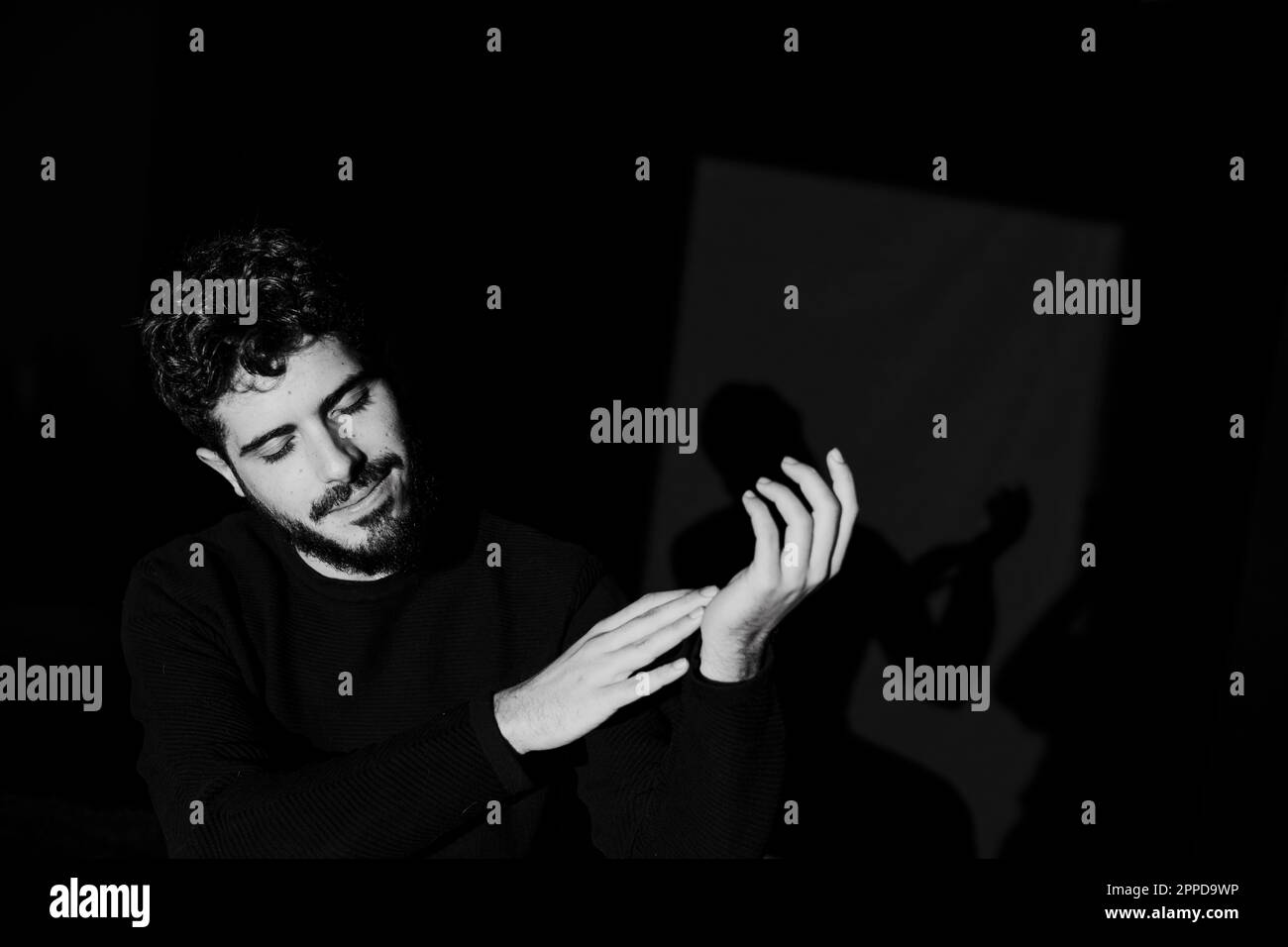 Giovane uomo sorridente che tocca le mani su sfondo nero Foto Stock