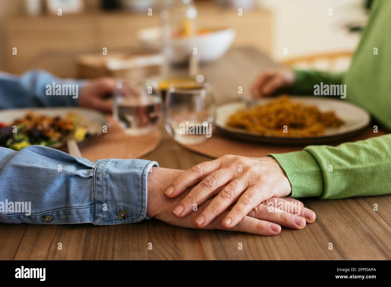 Donna anziana che si accatastano mano sull'uomo al tavolo da pranzo Foto Stock