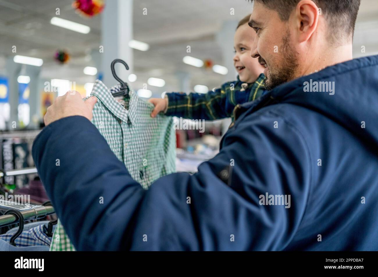 Uomo sorridente con figlio che sceglie i vestiti in deposito Foto Stock