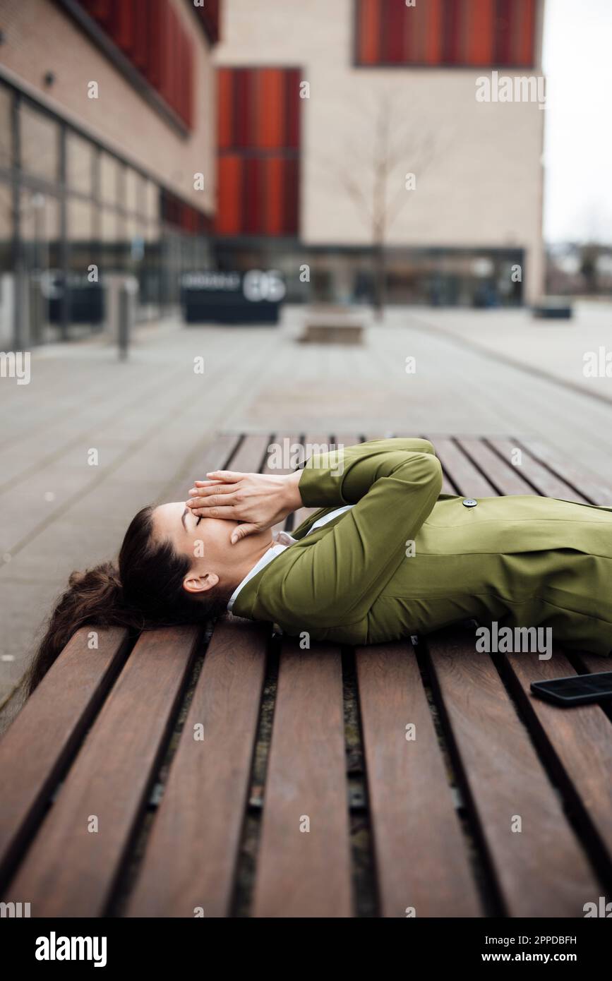 Donna d'affari che copre la bocca con mano su panca Foto Stock