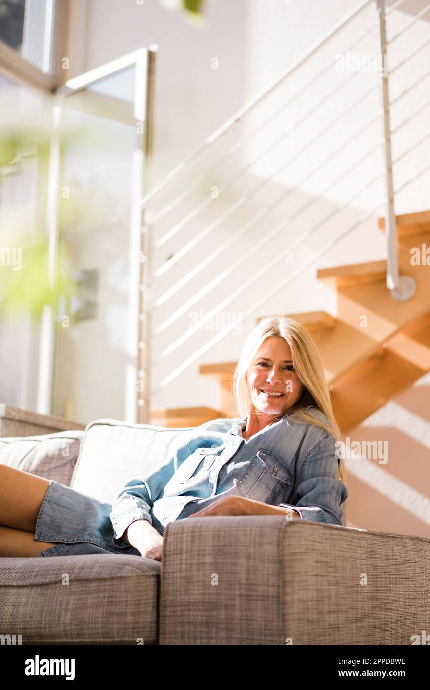 Felice donna matura che riposa sul divano a casa Foto Stock