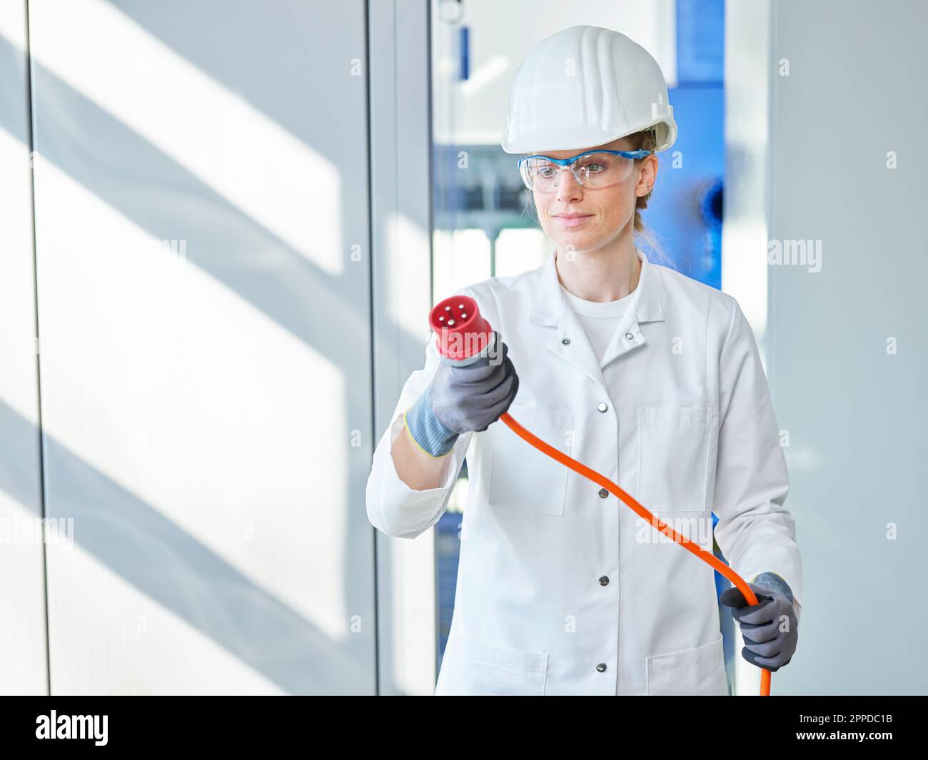 Donna che indossa un camice da laboratorio che esamina la spina di alimentazione in laboratorio Foto Stock