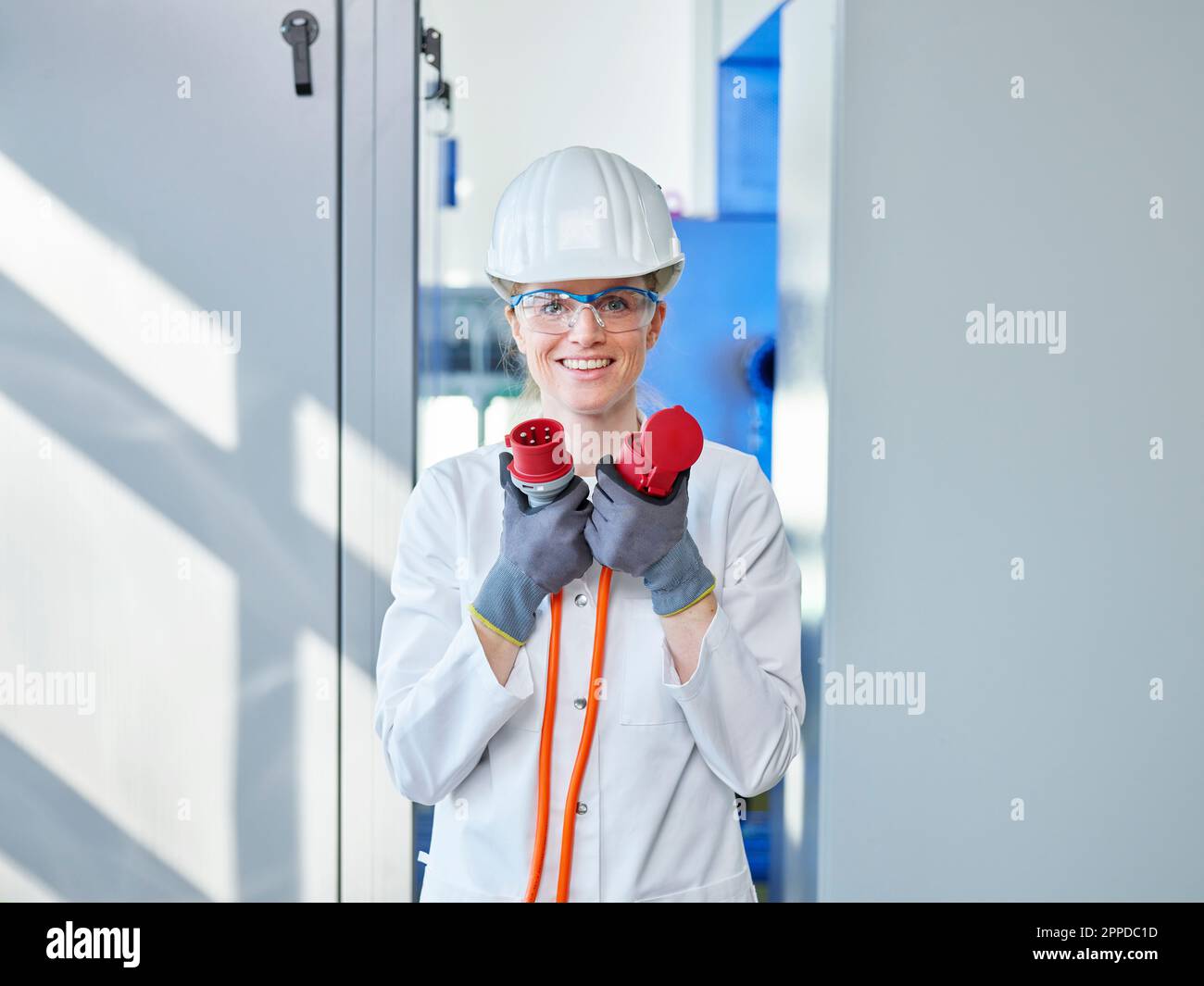 Donna felice che indossa un camice da laboratorio per l'analisi della spina di alimentazione in laboratorio Foto Stock