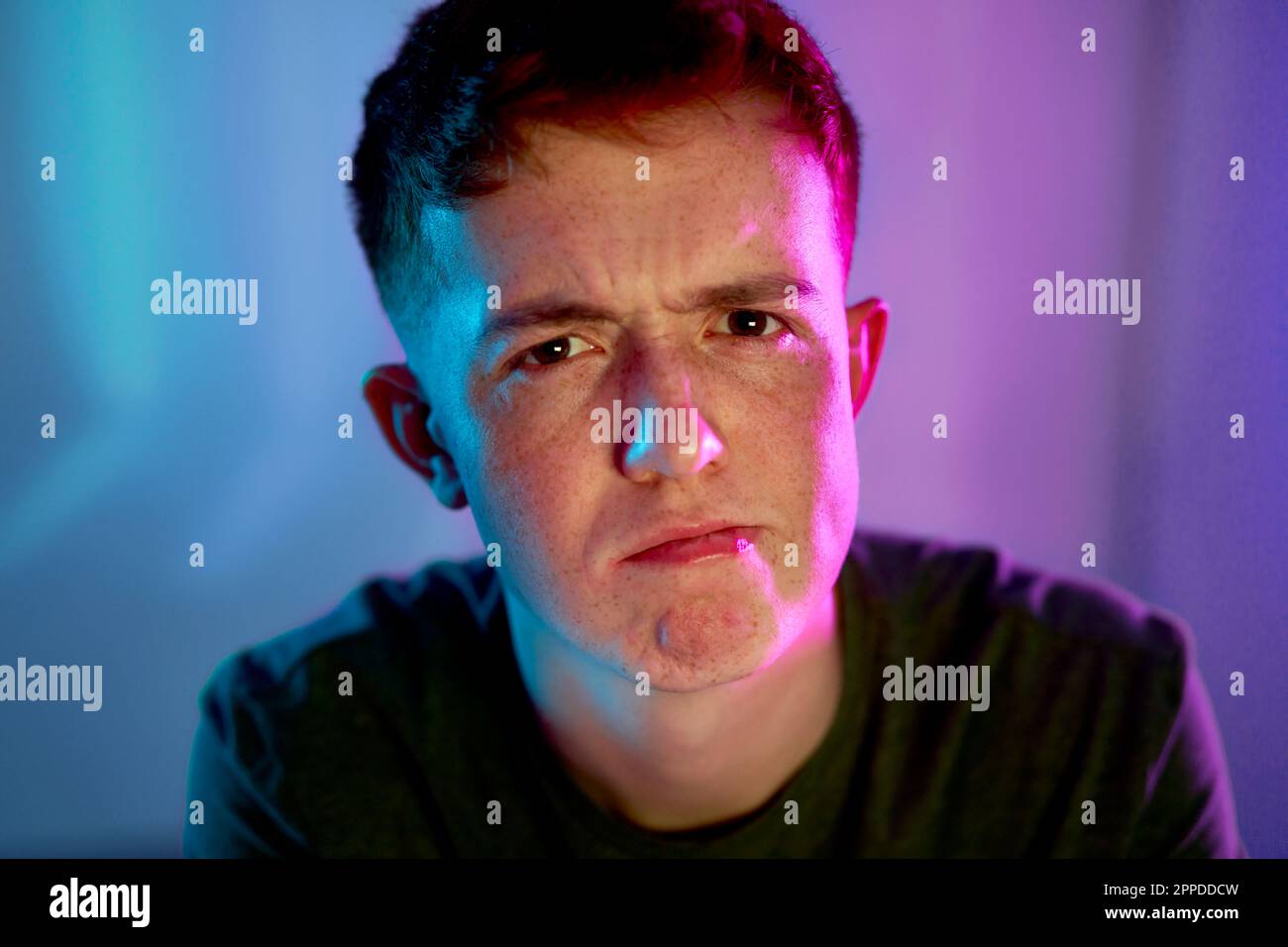 Giovane uomo con espressione facciale con luce al neon illuminata sul viso Foto Stock