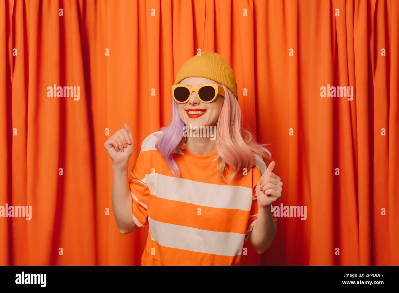 Donna felice con pugni clenched che ballano di fronte al sipario arancione Foto Stock
