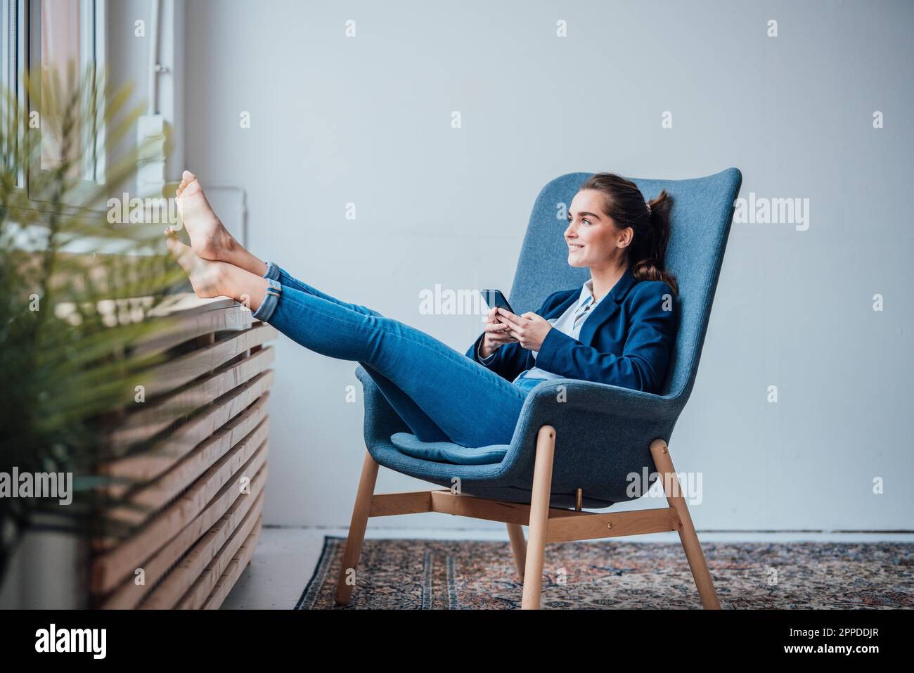 Felice giovane donna d'affari che tiene lo smartphone seduto in poltrona Foto Stock