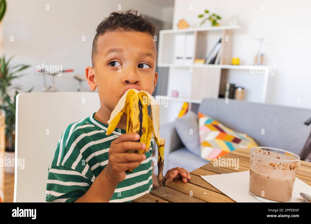 Ragazzo premuroso che mangia banana a casa Foto Stock