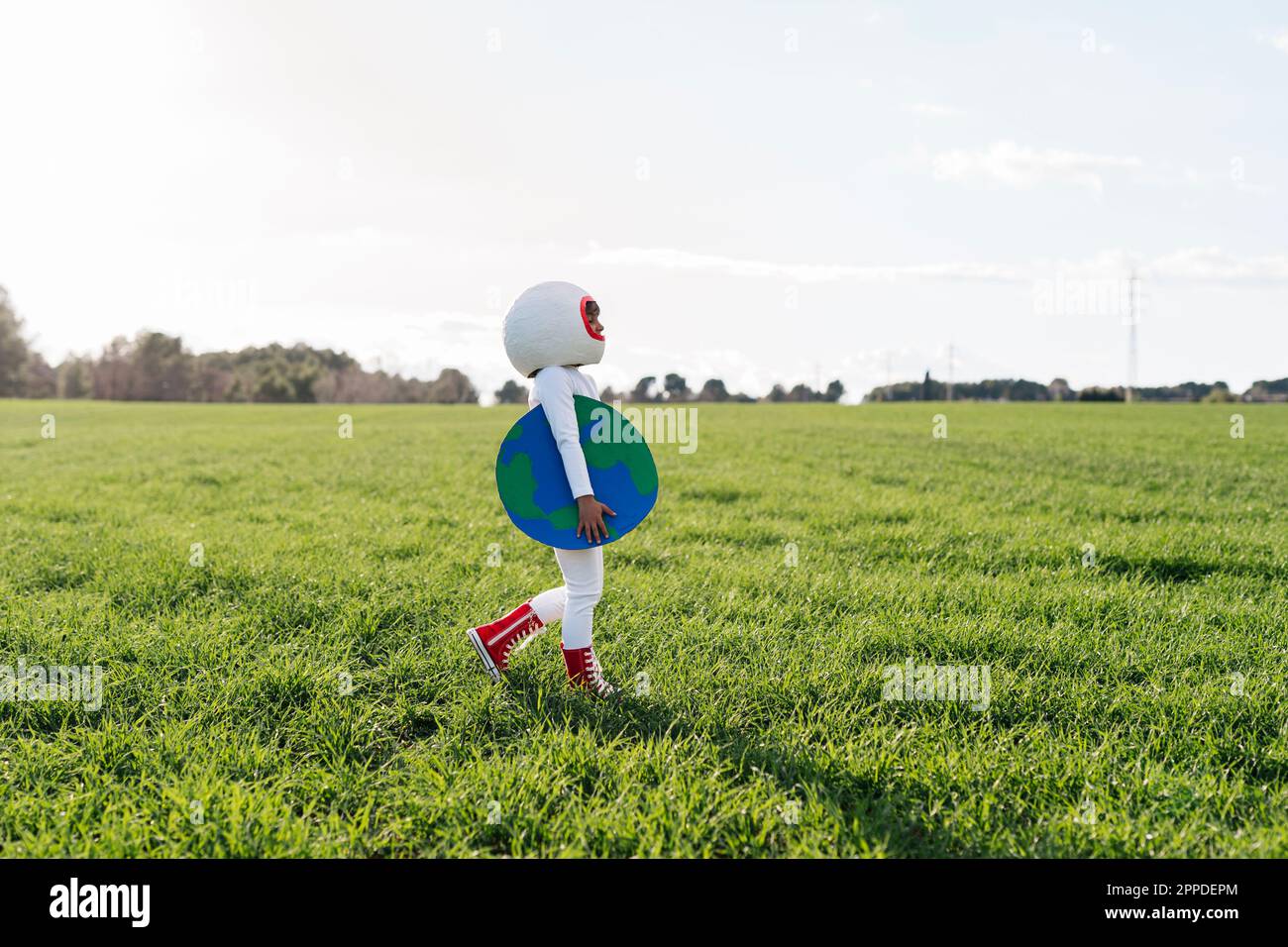 Ragazza vestita come astronauta camminare con terra tagliata su erba Foto Stock