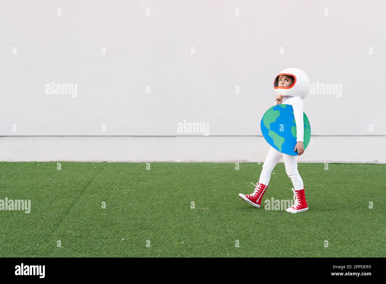 Ragazza che indossa costume astronauta tenendo la terra tagliata a piedi su erba Foto Stock