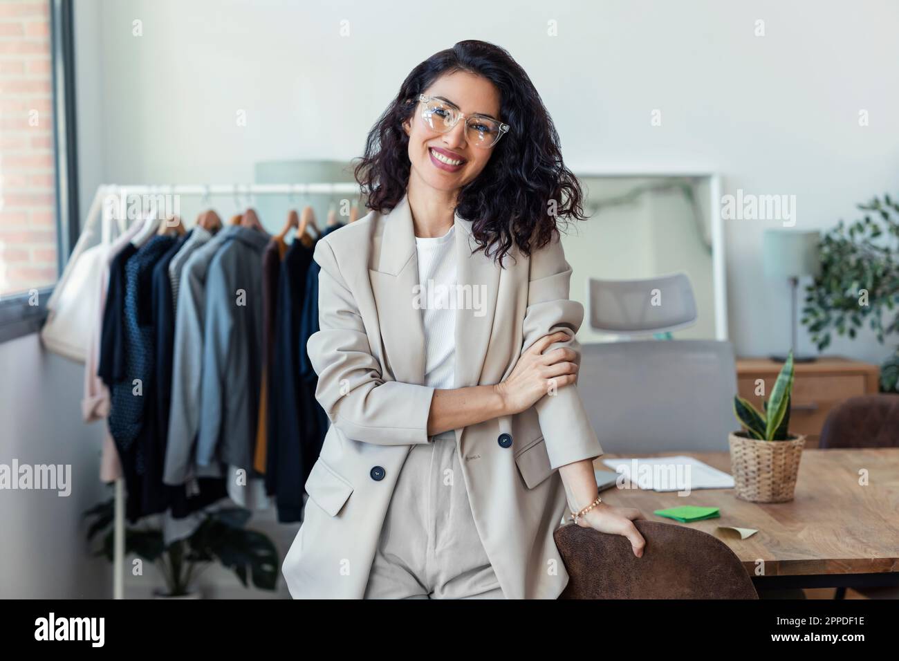 Buon designer di moda che indossa occhiali appoggiati dalla scrivania in studio Foto Stock