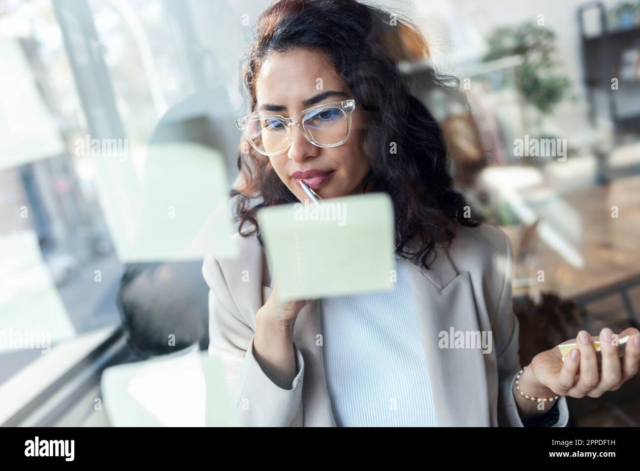 Stilista attento che guarda le note adesive sulla parete di vetro Foto Stock