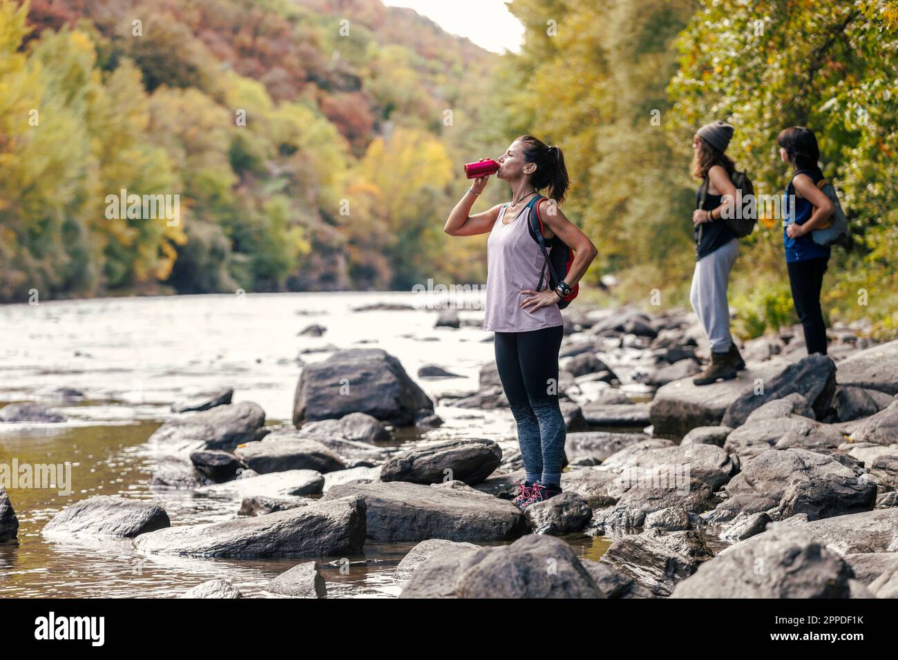 Donna che beve acqua dalla bottiglia con le figlie in piedi sullo sfondo Foto Stock