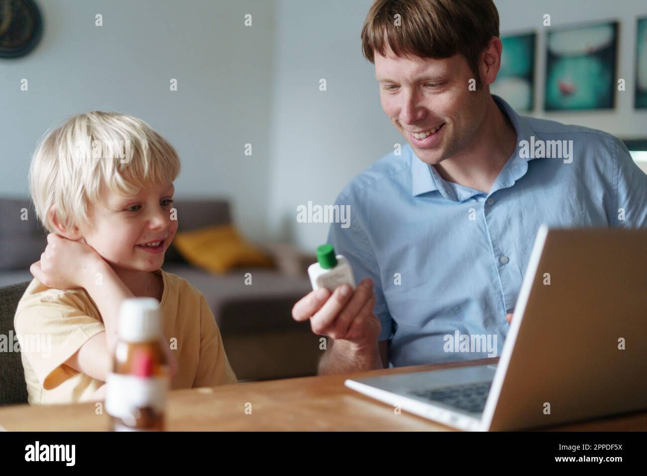 Figlio sorridente con padre che sceglie la medicina per la varicella Foto Stock