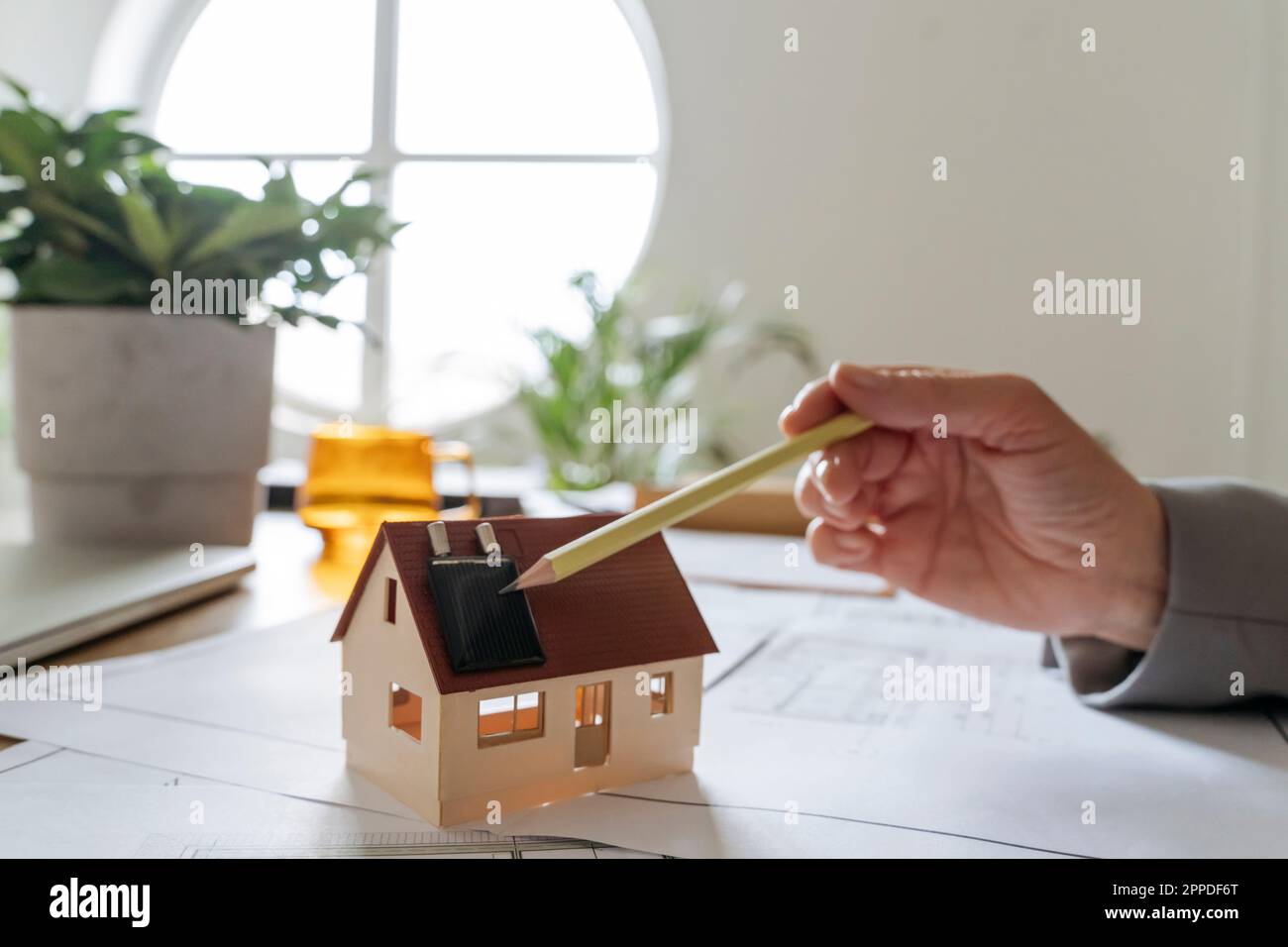 Mano di agente immobiliare con modello di casa che punta matita su pannello solare Foto Stock