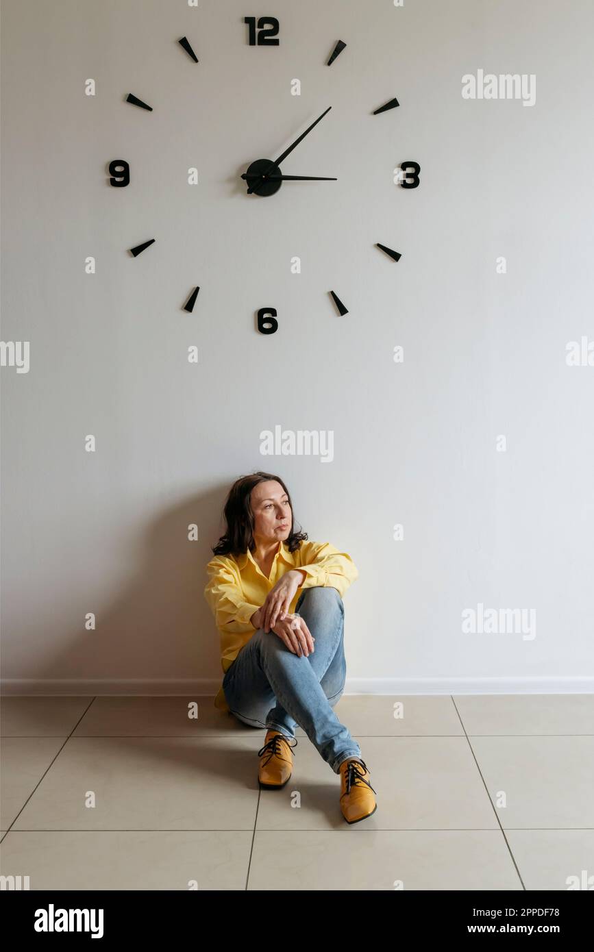 Donna premurosa seduta sotto l'orologio sul pavimento Foto Stock