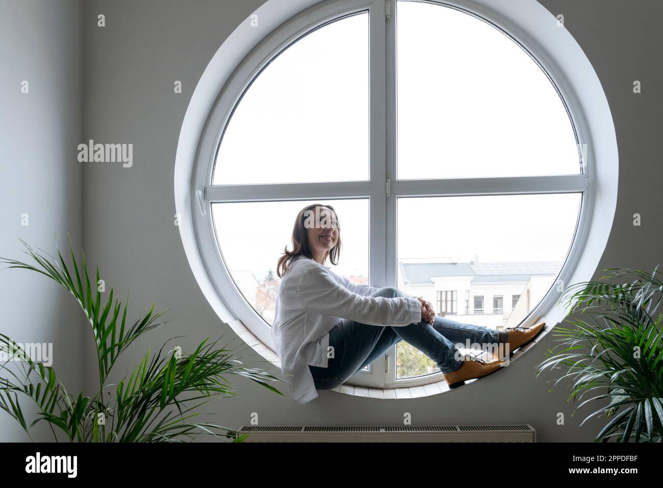 Donna d'affari premurosa seduta sul davanzale rotondo della finestra di forma Foto Stock