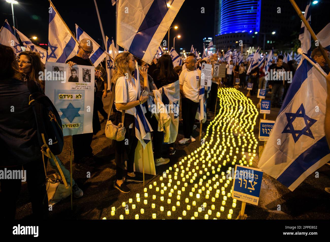 Tel Aviv, Israele. 22nd Apr, 2023. I membri della famiglia in lutto tengono cartelloni con foto dei loro cari, accanto a migliaia di candele Yom HaZikaron per il Memorial Day dei soldati caduti israeliani e le vittime degli attacchi terroristici durante una manifestazione di revisione anti-giudiziaria a Tel Aviv. Credit: SOPA Images Limited/Alamy Live News Foto Stock