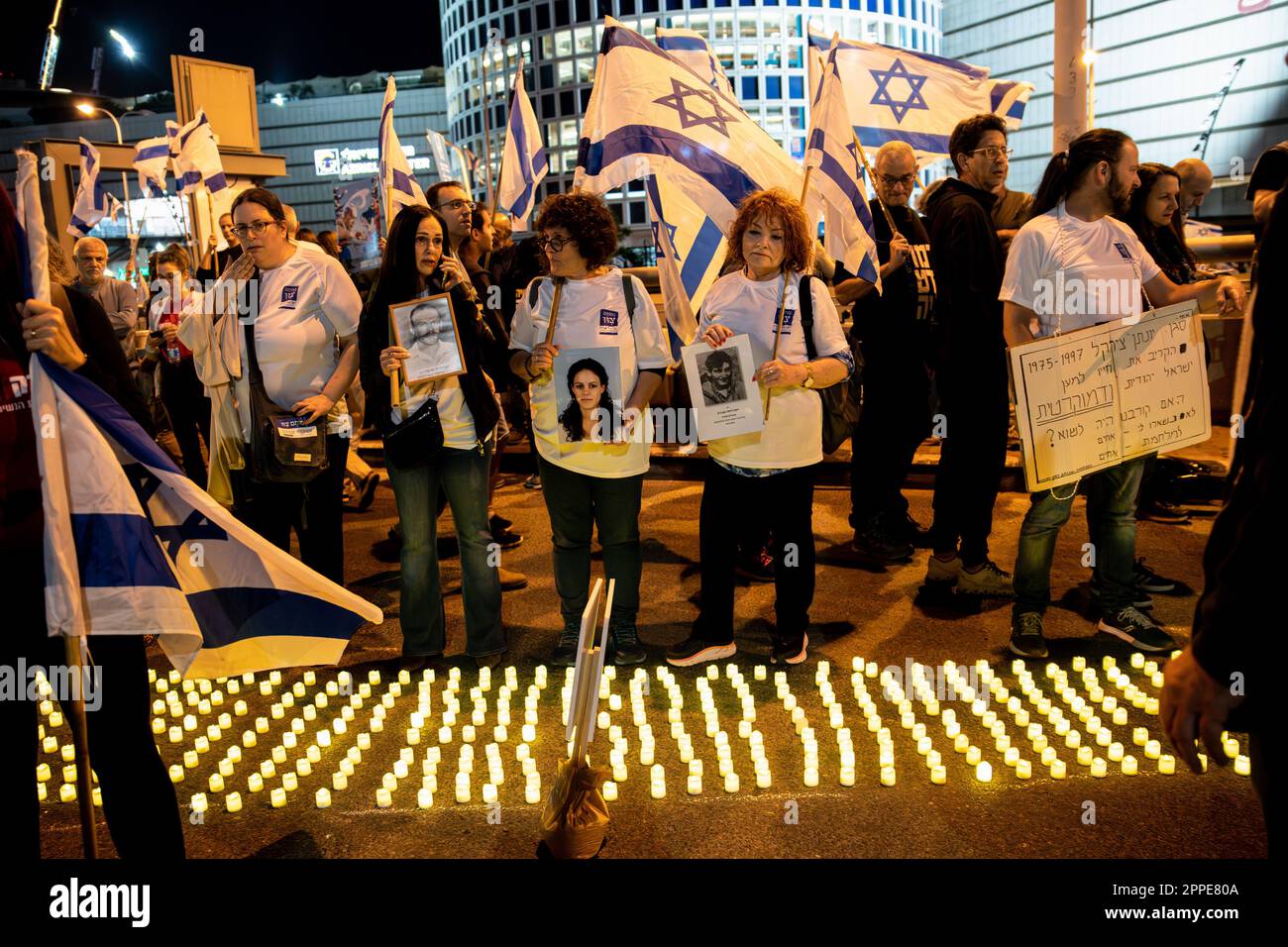 Tel Aviv, Israele. 22nd Apr, 2023. I membri della famiglia in lutto tengono cartelloni con foto dei loro cari, accanto a migliaia di candele Yom HaZikaron per il Memorial Day dei soldati caduti israeliani e le vittime degli attacchi terroristici durante una manifestazione di revisione anti-giudiziaria a Tel Aviv. Credit: SOPA Images Limited/Alamy Live News Foto Stock