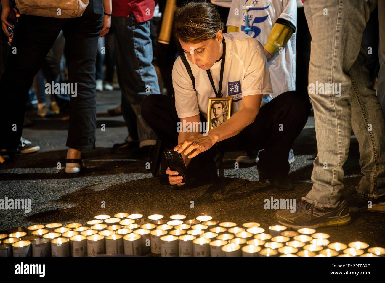 Tel Aviv, Israele. 22nd Apr, 2023. I membri della famiglia in lutto tengono cartelloni con foto dei loro cari, accanto a migliaia di candele Yom HaZikaron per il Memorial Day dei soldati caduti israeliani e le vittime degli attacchi terroristici durante una manifestazione di revisione anti-giudiziaria a Tel Aviv. Credit: SOPA Images Limited/Alamy Live News Foto Stock