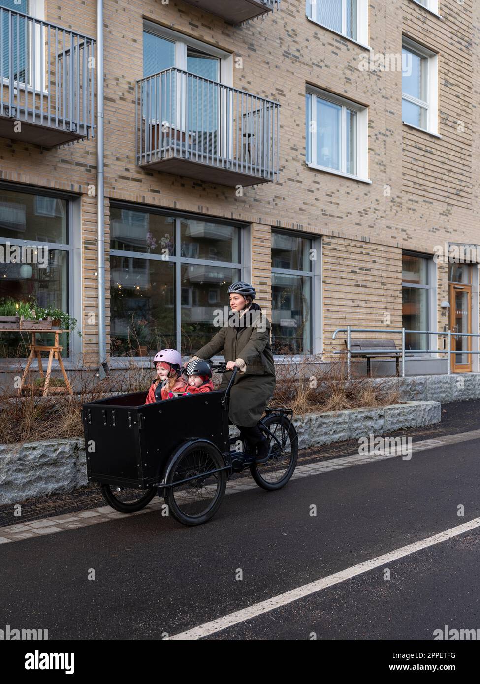 Giovane madre in bicicletta con due bambini in bicicletta da carico Foto Stock