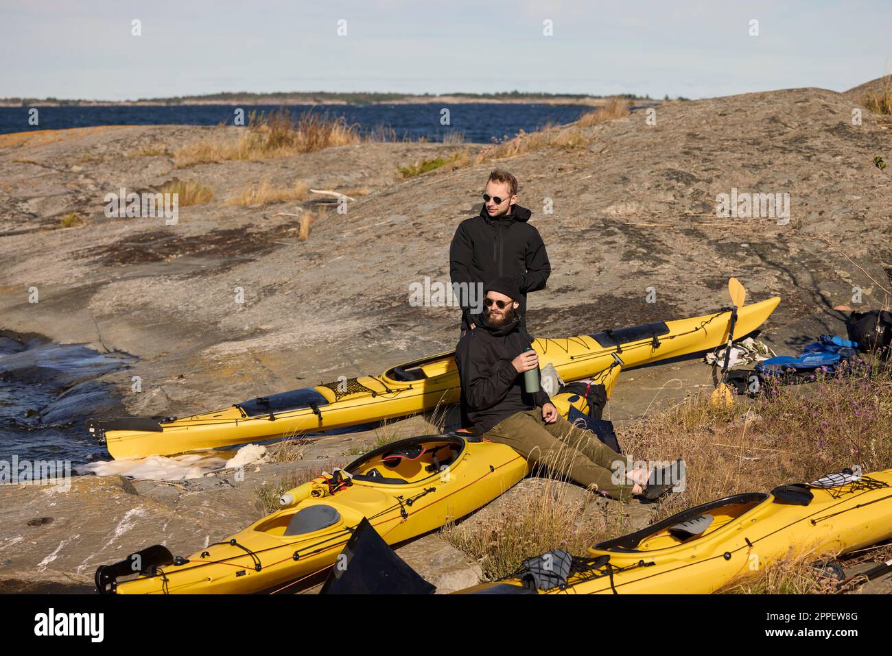 Uomini seduti vicino a kayak sulla costa rocciosa Foto Stock