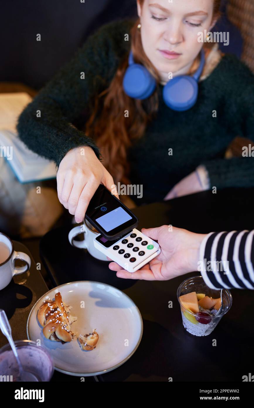 Giovane donna che paga con il telefono nel caffè Foto Stock