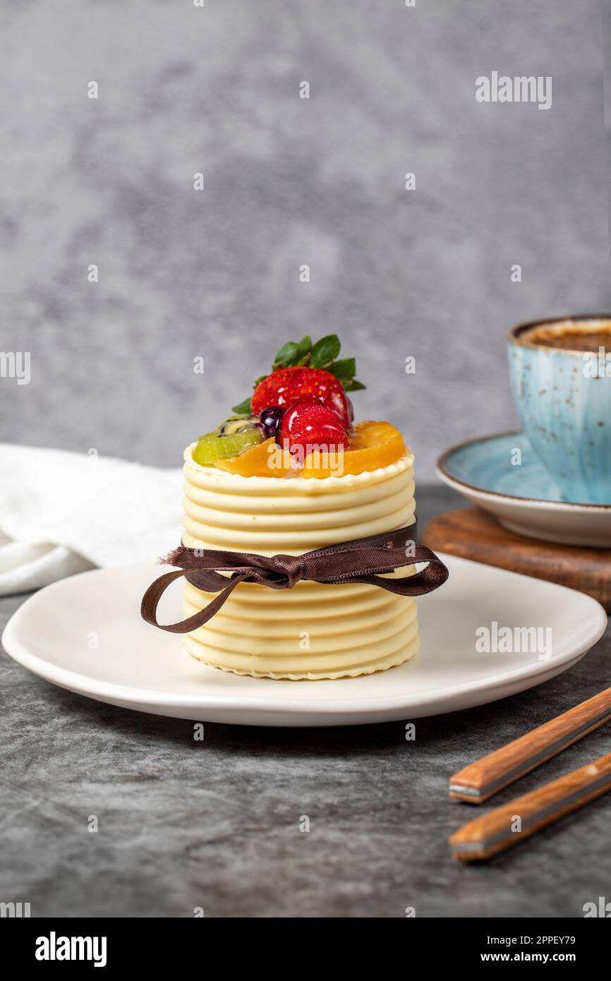 Torta alla crema di frutta. Torta di fragole, pere, kiwi e lamponi ricoperta di cioccolato bianco su fondo scuro. Dolci di pasticceria Foto Stock