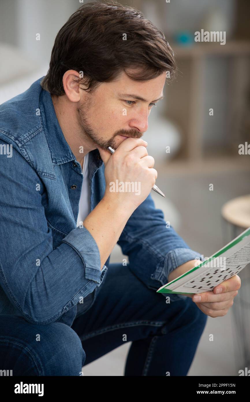 giovane uomo seduto sul divano e facendo cruciverba puzzle Foto Stock