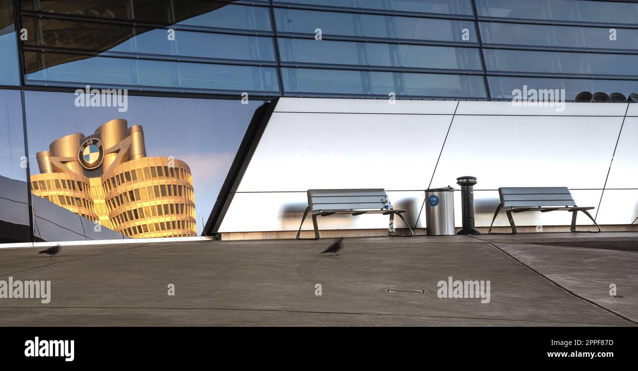 Parcheggio di fronte ad un edificio moderno, sulla facciata del quale si riflette un grattacielo con il logo BMW.cgi produzione backplate Foto Stock