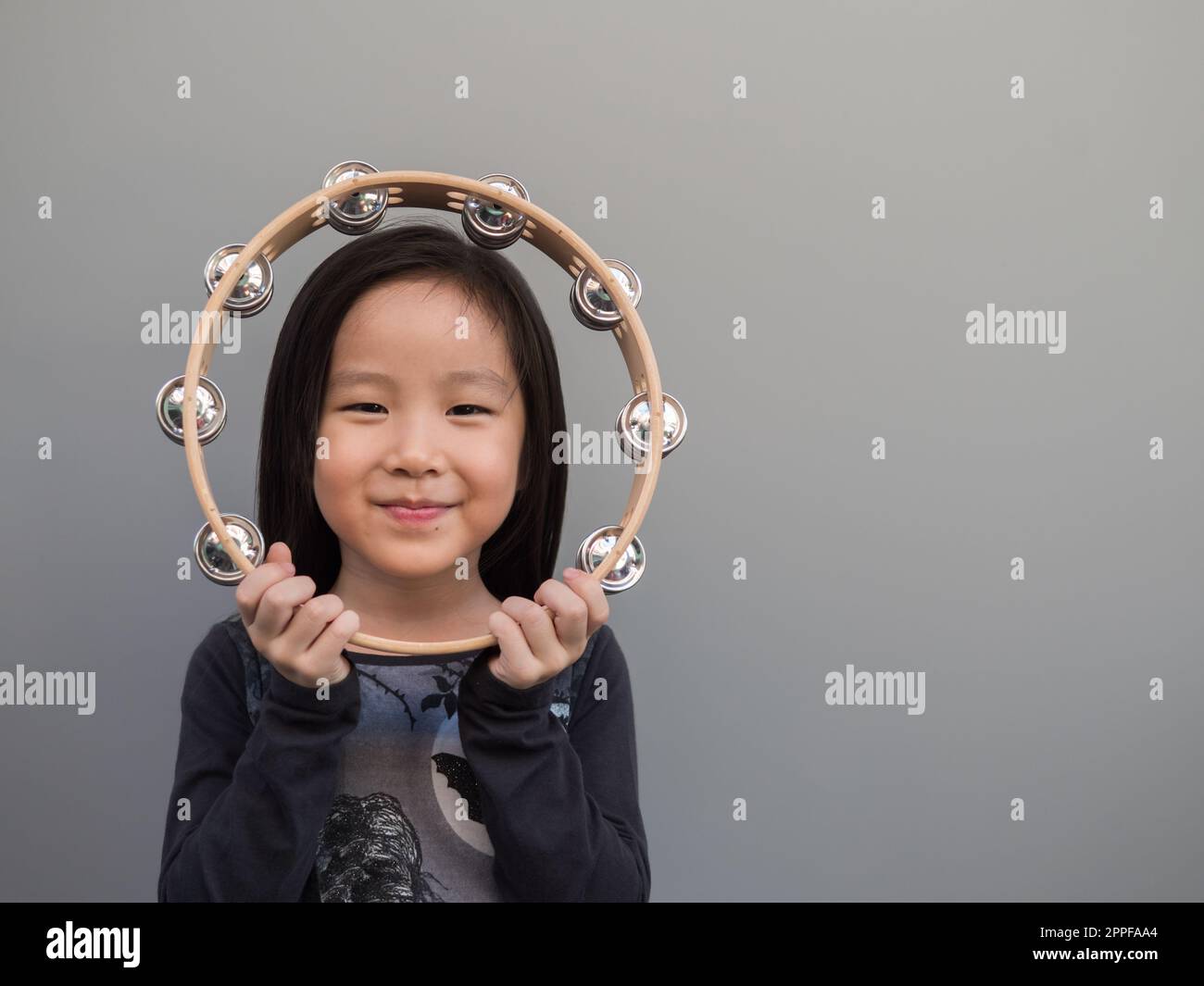 Piccolo bambino asiatico giocare il tamburello, sfondo grigio Foto Stock