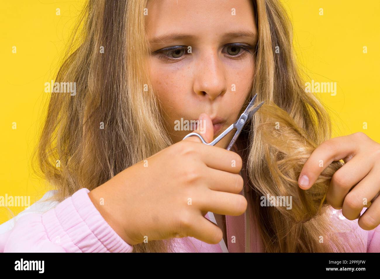 Bambino adorabile ragazza parrucchiere taglio capelli biondi lunghi con forbici metalliche sul giallo Foto Stock