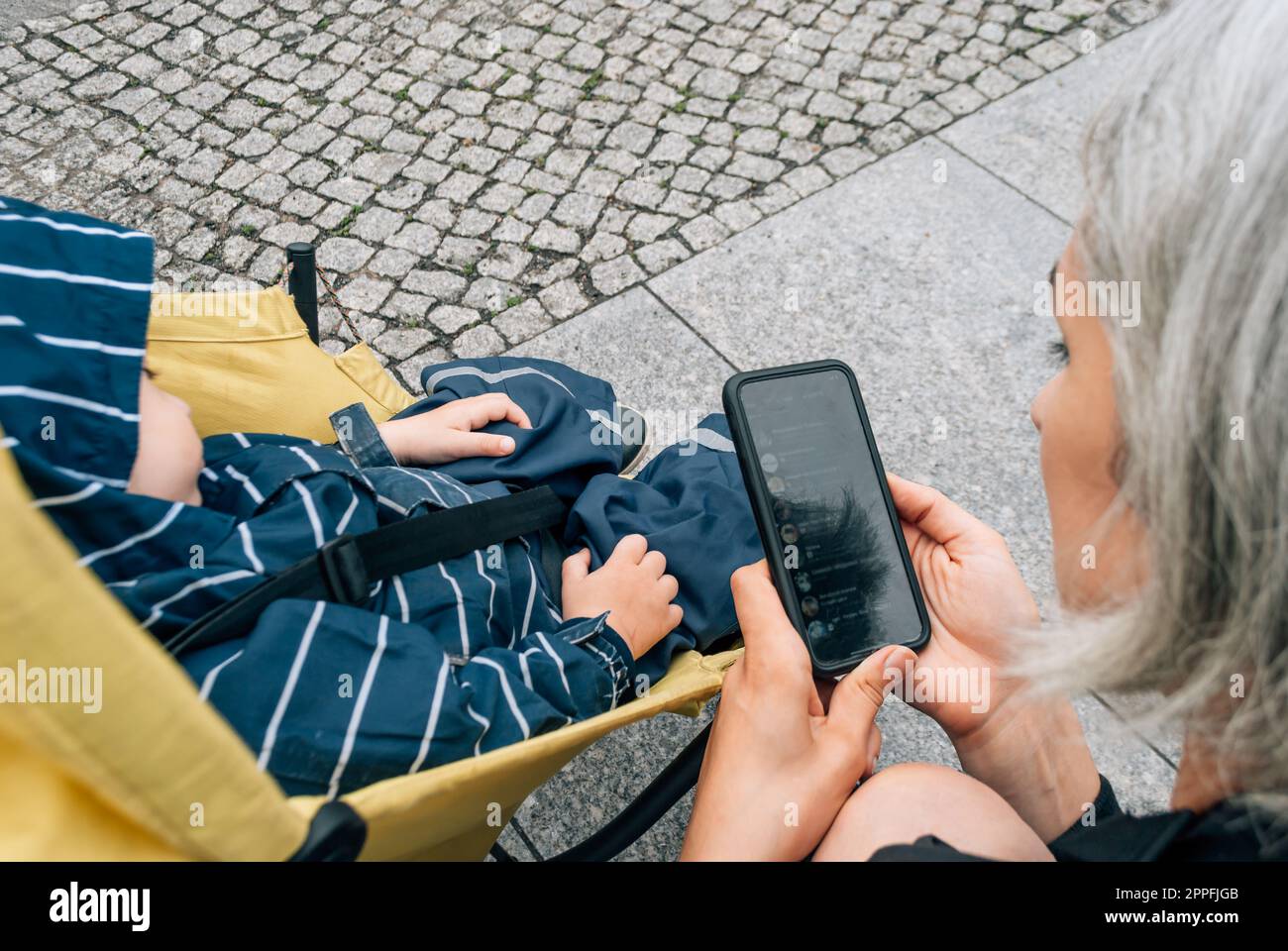 La mamma usa un messaggero sul suo cellulare vicino al passeggino con suo figlio addormentato Foto Stock