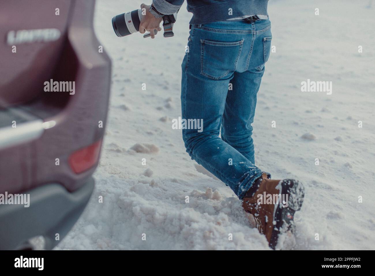 Un maschio di mezza età con una macchina fotografica cammina attraverso la neve. Foto Stock