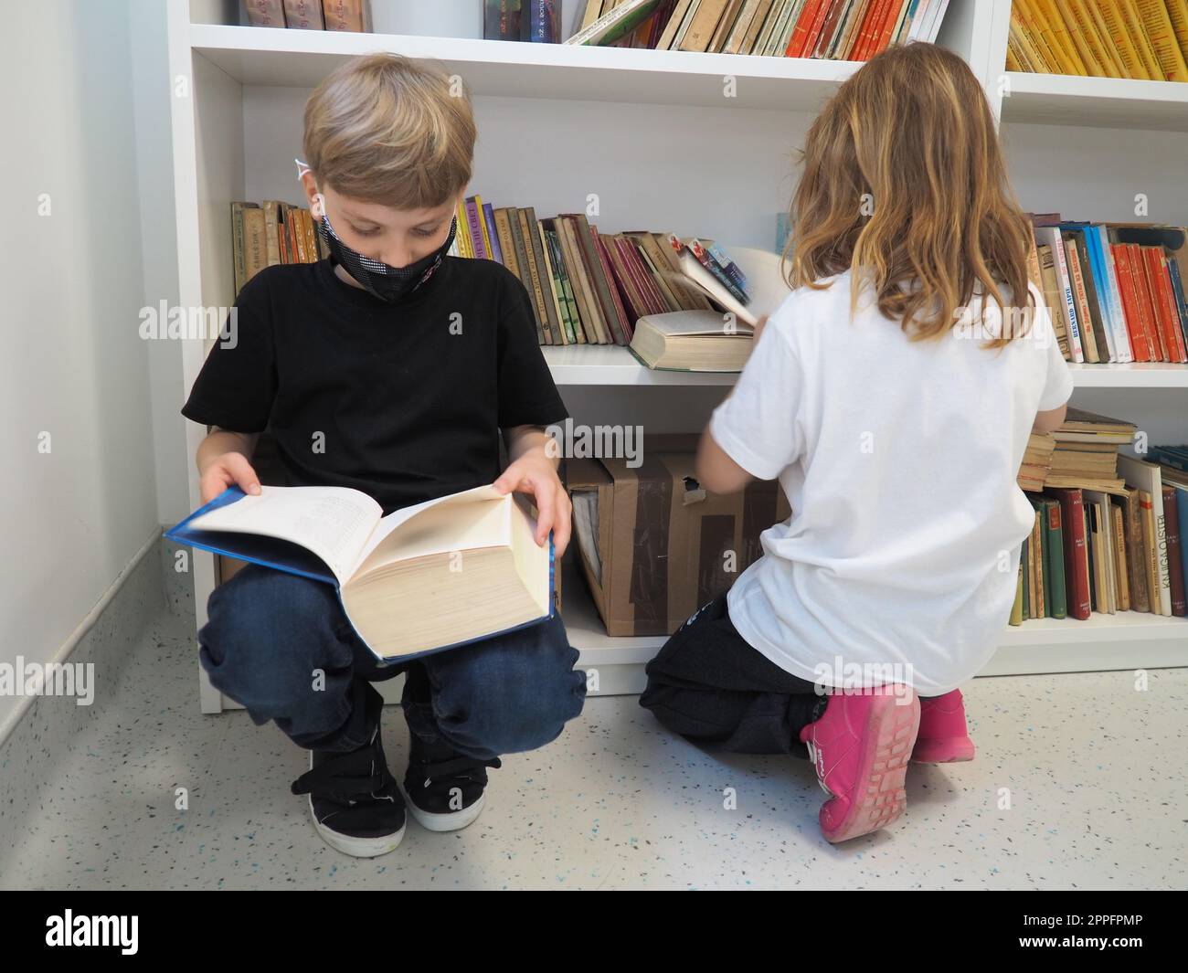 Sremska Mitrovica, Serbia, 15 maggio 2021 bambini nella biblioteca scolastica. Un ragazzo e una ragazza cercano e sfogliano i libri nel rack della biblioteca. Il ragazzo sta leggendo un libro molto denso. A scuola. Gli adolescenti studiano Foto Stock