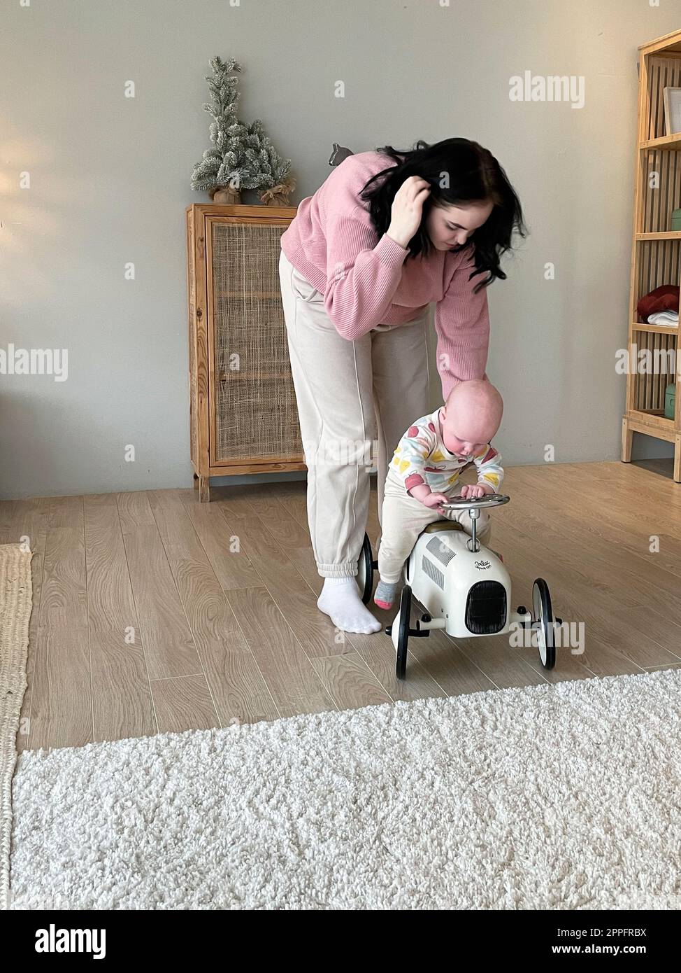 La giovane madre tiene la figlia seduta su un'auto di legno giocattolo Foto Stock