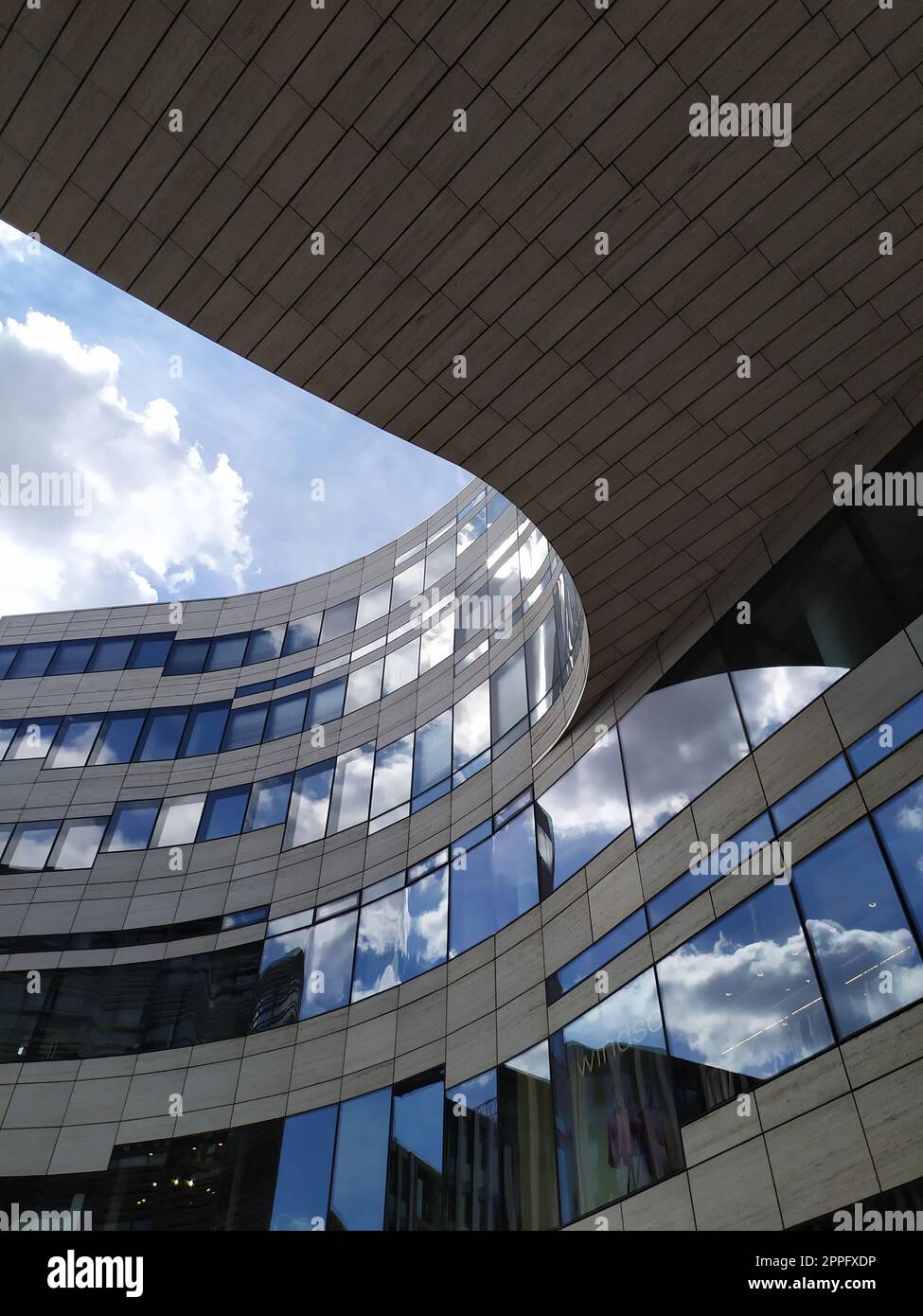 Dusseldorf, Germania - 16 luglio 2022: L'architettura moderna del DÃ¼sseldorfer KÃ¶bogen in estate mostra una facciata in vetro attraente e stravagante di un centro commerciale organico e curvo con nuvole blu Foto Stock