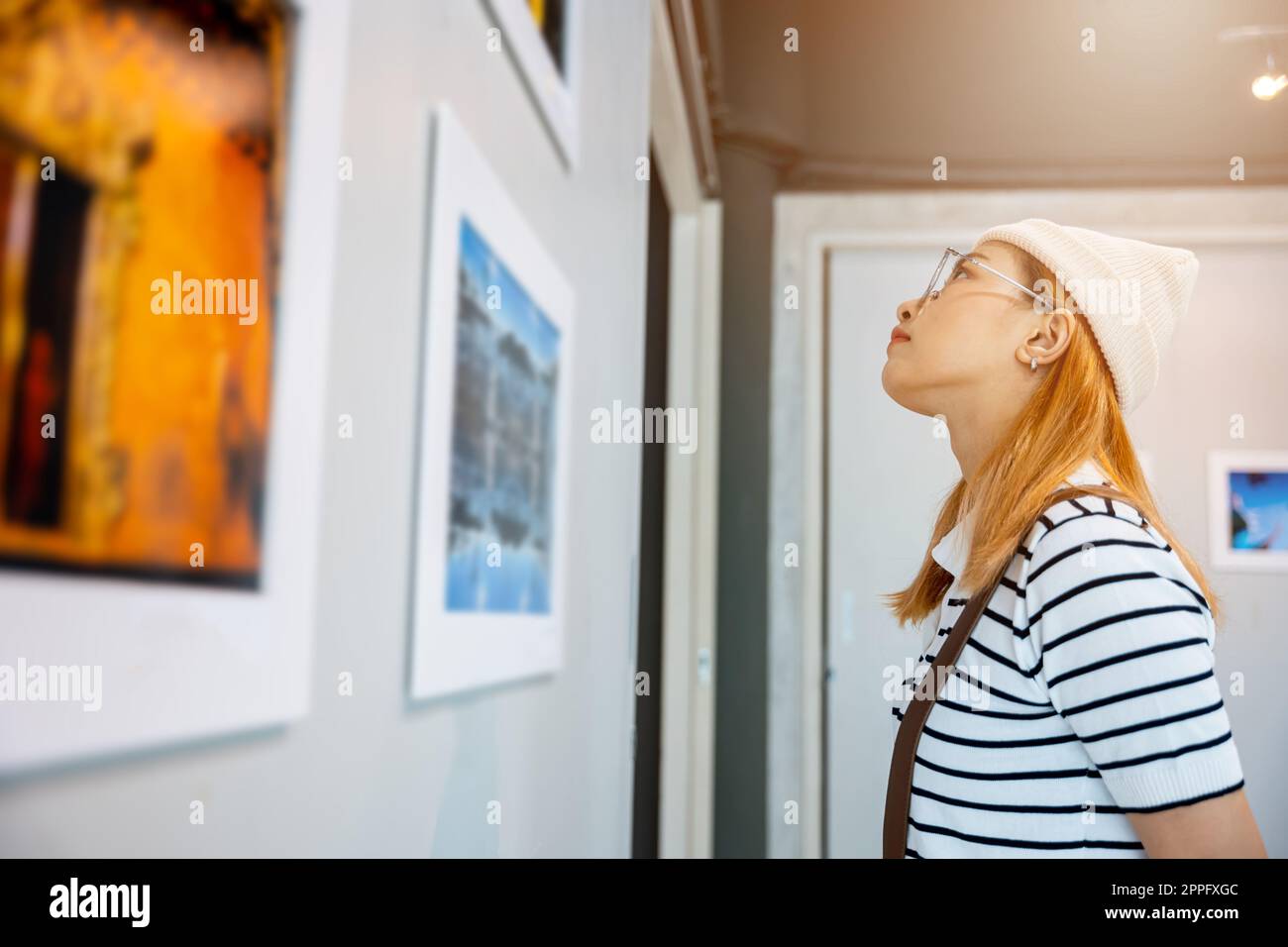 Donna asiatica che guarda una galleria d'arte di fronte a quadri colorati incorniciati Foto Stock