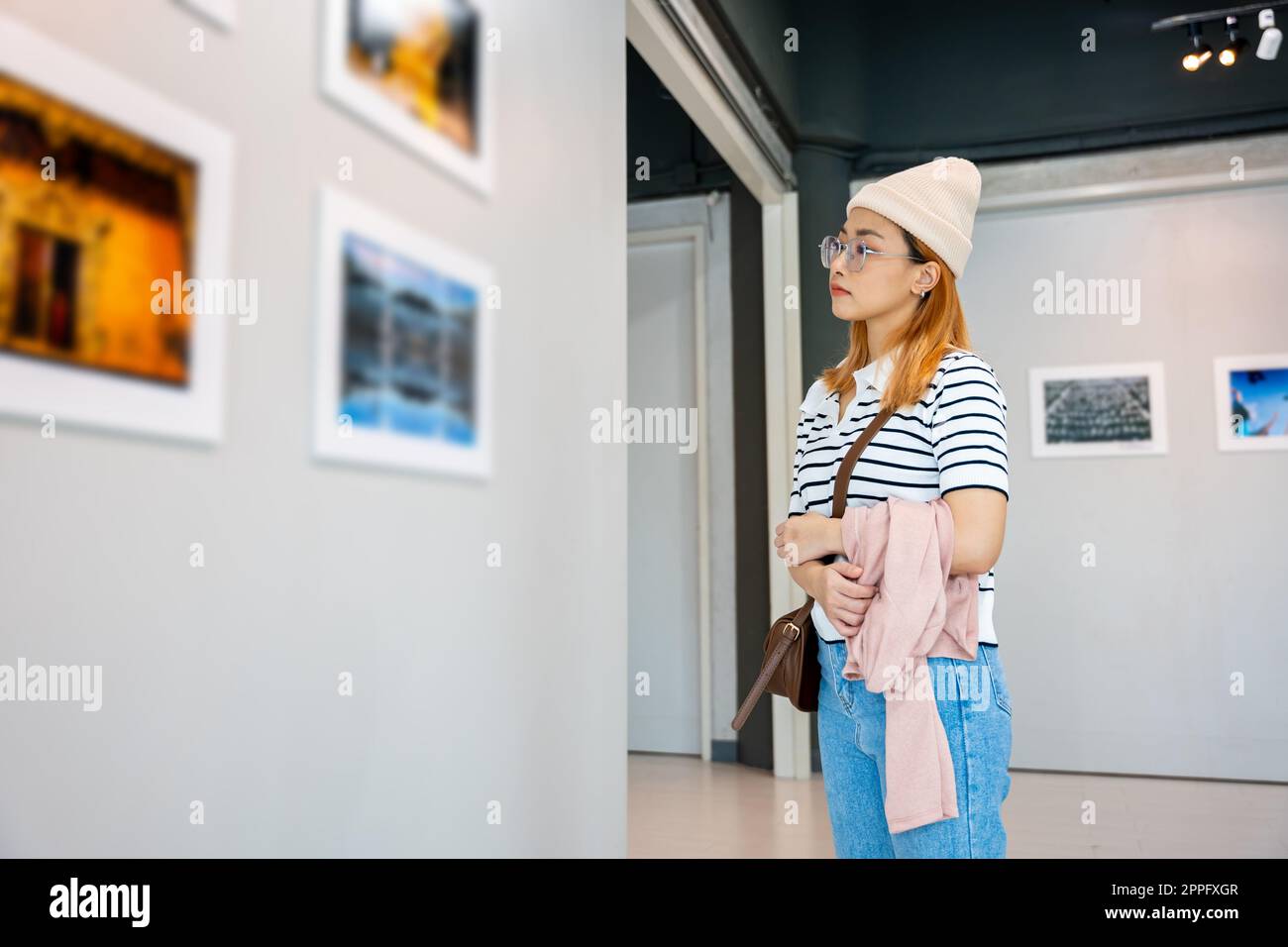 Donna in piedi che guarda una collezione di gallerie d'arte davanti a quadri incorniciati Foto Stock