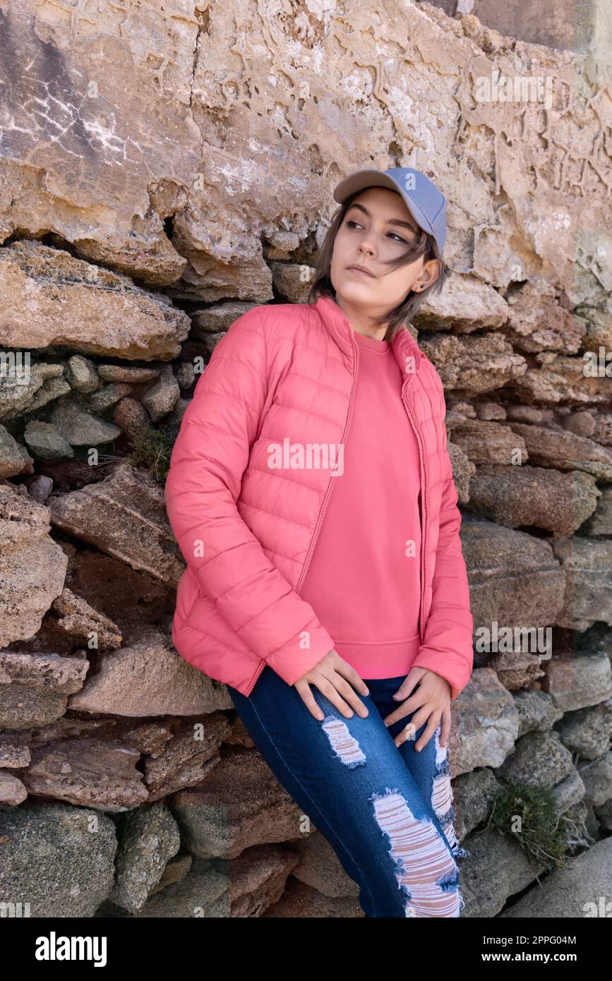 Ragazza adolescente seria che indossa una camicia rosa e un razzo con pudded in piedi all'aperto vicino a un muro, mockup Foto Stock