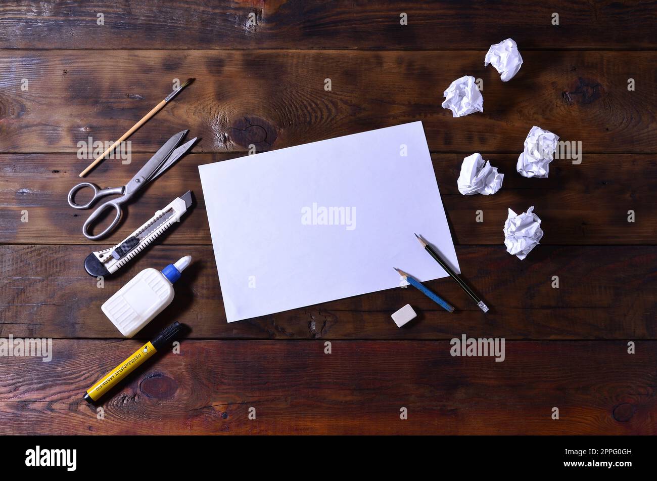 Una scuola o un ufficio ancora in vita con un foglio bianco di carta e molte forniture per ufficio. Le forniture scolastiche giacciono su uno sfondo di legno marrone. Posiziona per il testo Foto Stock