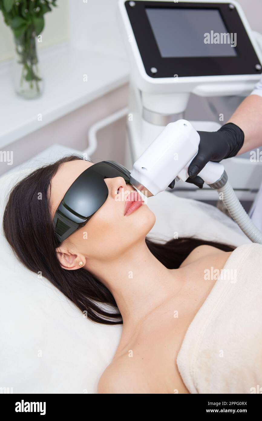 Il processo di depilazione laser del corpo femminile. cosmetologia professionale, epilazione della zona del viso e del labbro superiore. Ragazza con gli occhiali. Concetto di cura del corpo. Foto Stock